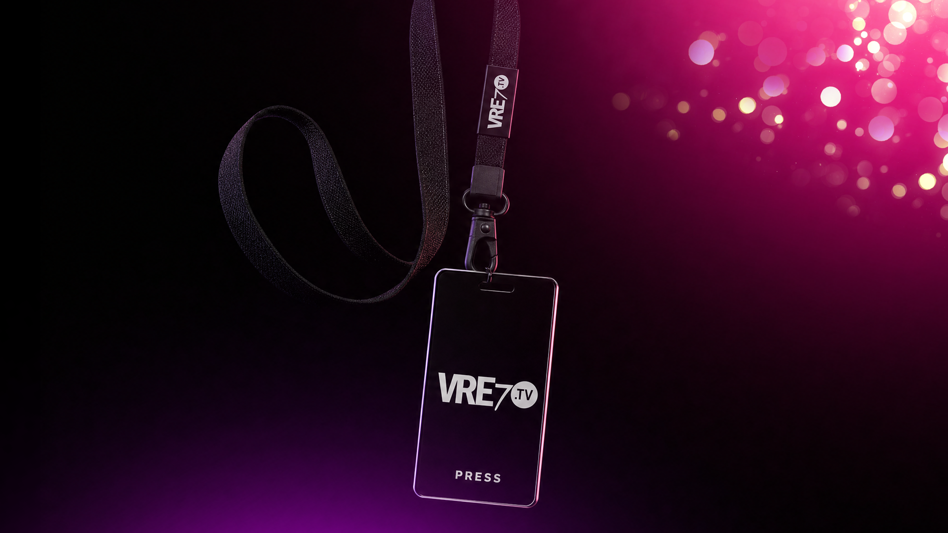 A VRE7 TV press badge on a black lanyard against a dark backdrop with pink bokeh light